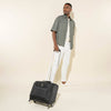 lifestyle view of a man pulling the black travelpro maxlite 5 carry-on rolling tote by its extended powerscope lite handle, demonstrating its compact size and mobility for short trips.