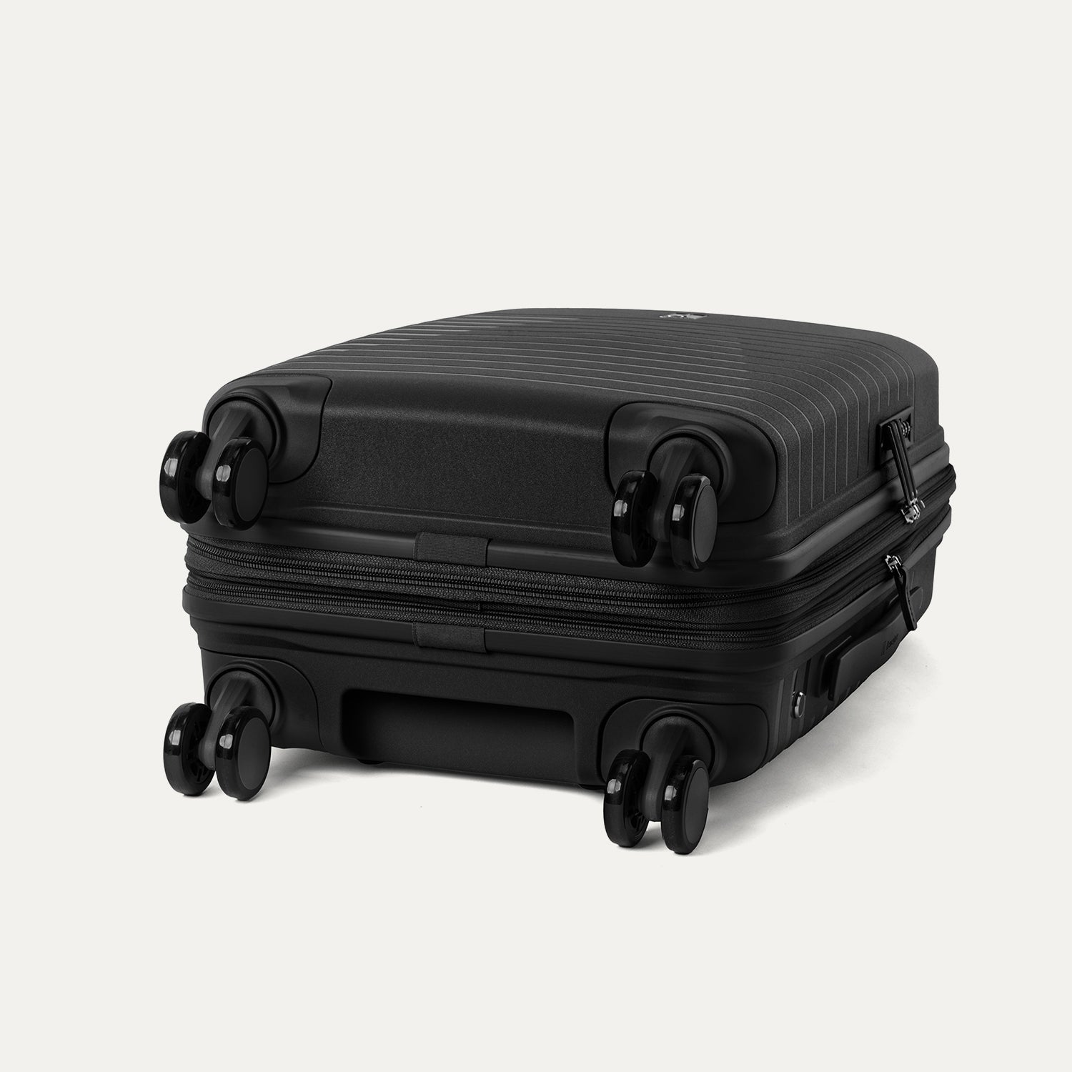 Side-profile view of the Optima Expandable Compact Carry-on Spinner in Black, highlighting the base construction and the self-aligning MagnaTrac® spinner wheels that ensure smooth, drift-free mobility.